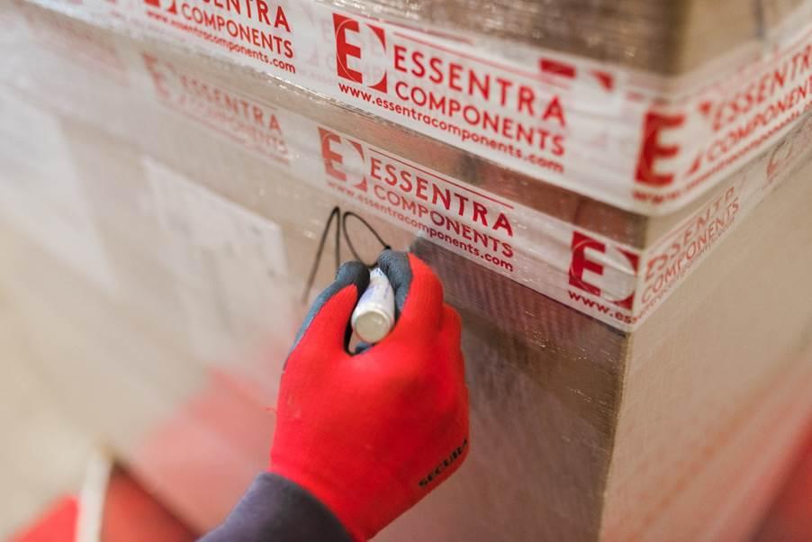 A person wearing red gloves marks a cardboard box sealed with Essentra Components tape, using a black marker.