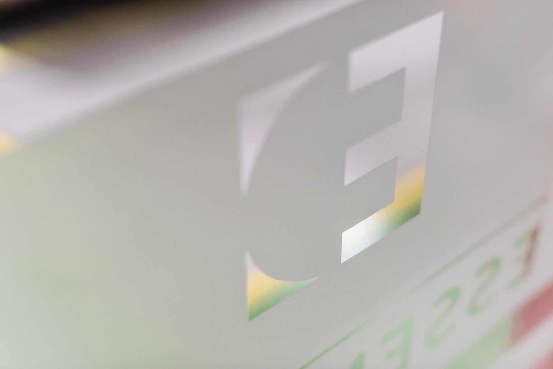 Close-up of a frosted glass panel with a cut-out "E" shape, revealing a blurred, colorful background.